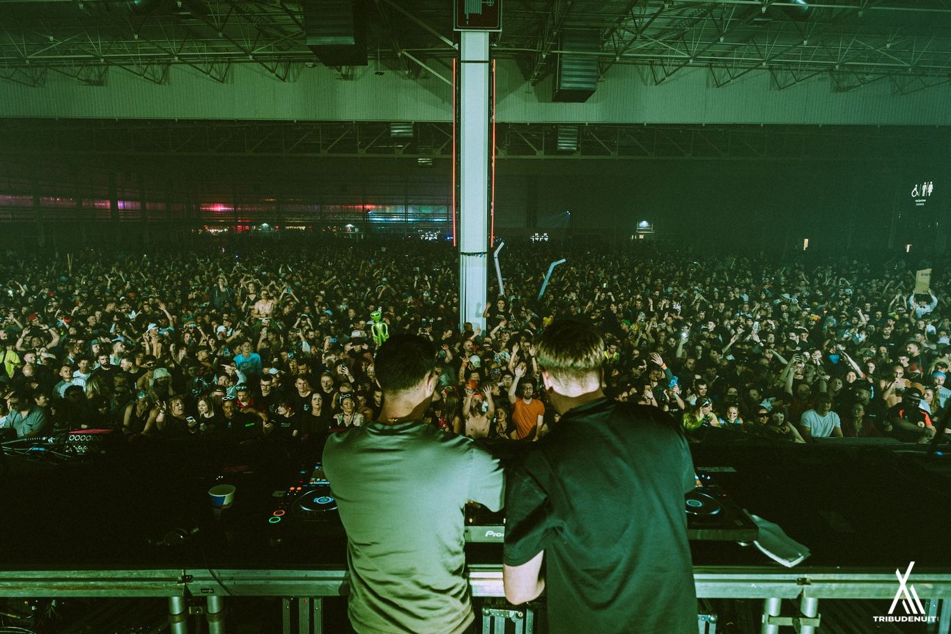 Deux personnes de dos aux platines face à une foule compacte dans une salle éclairée de vert – DREAM NATION FESTIVAL